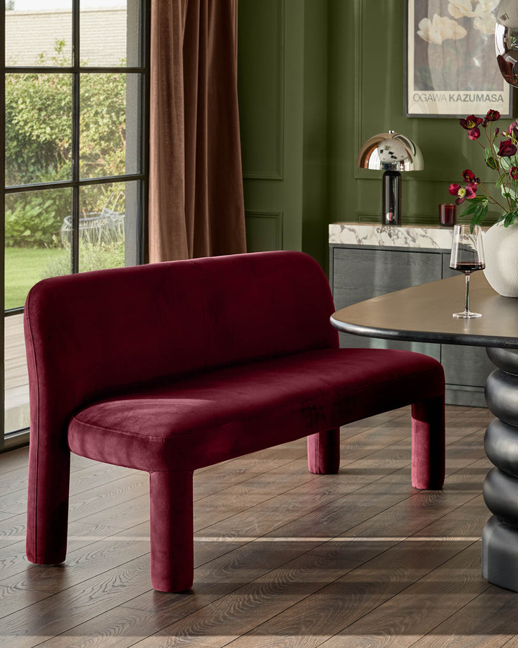 Mason 3-seater dining bench in plum velvet with curved backrest and cylindrical legs, positioned in green interior space.