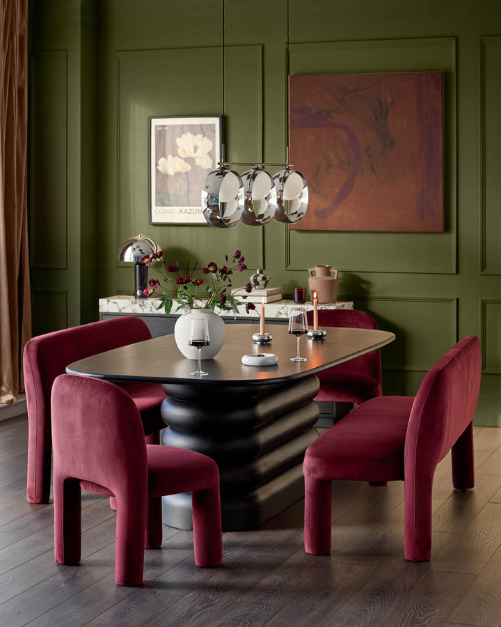 Mason 3-seater dining bench in plum velvet, shown in a modern dining setting with black table and green walls.
