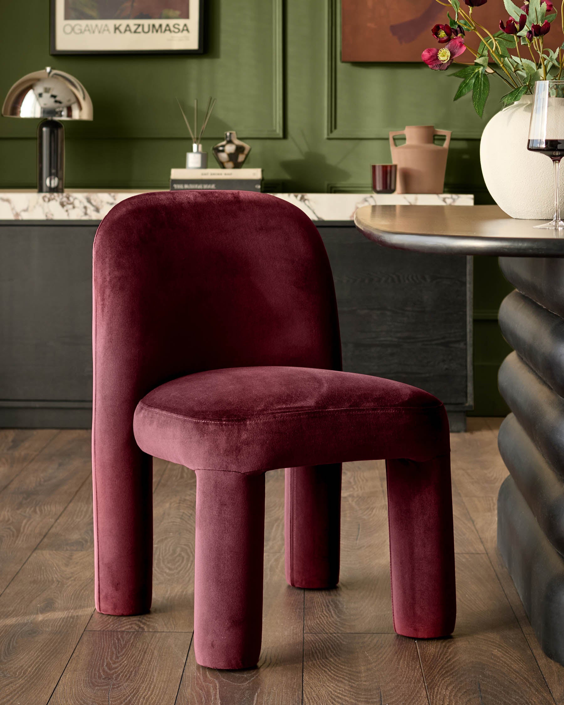 Mason dining chair in plum velvet, showcasing rounded sculptural form with curved back and cylindrical legs in a styled interior.