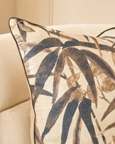 Madeira cushion in natural tones featuring dark blue and taupe leaf pattern on cream linen, displayed on beige upholstered furniture.
