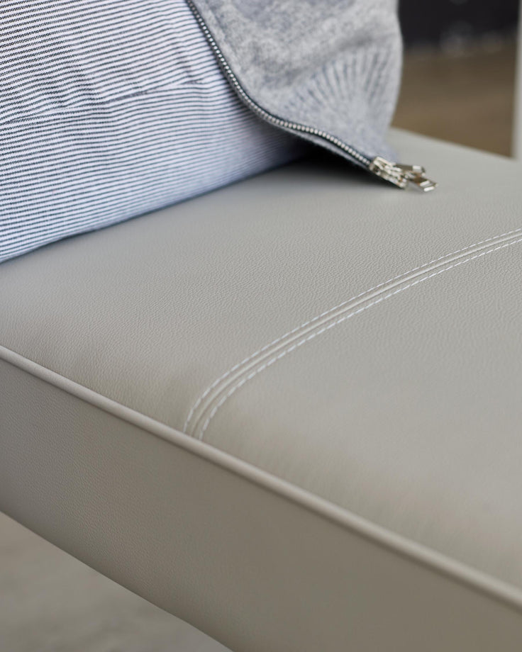 Close-up of a stylish grey leather bench seat with a striped cushion and grey zip-up top. Modern, minimalist design.