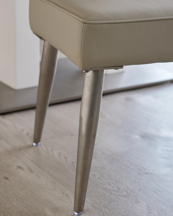 Close-up of a stool with a beige leather seat and brushed metal legs. Modern and stylish seating solution.