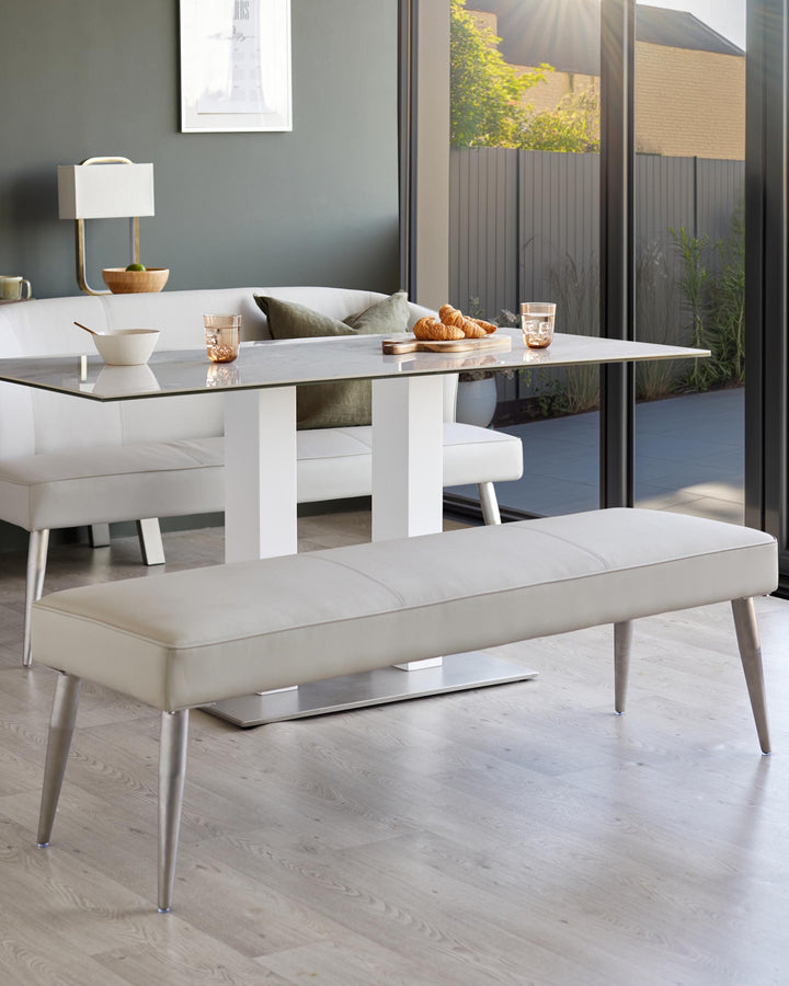 A modern dining set with a glass table, white bench seating and a separate light grey dining bench.