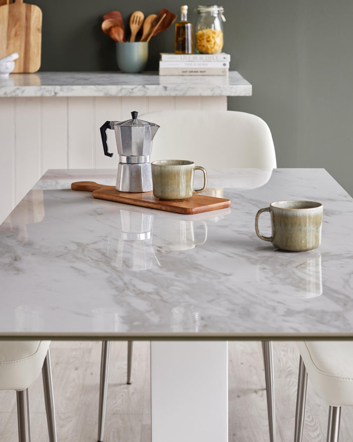 Marble table with coffee maker and cups, paired with stylish chairs. A modern and inviting kitchen setting.