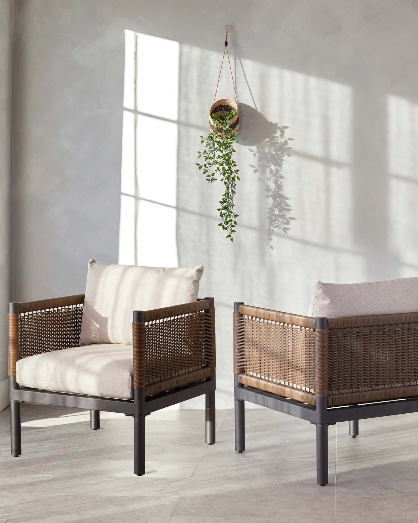 Two modern armchairs with dark wood frames and wicker backrests, complemented by light beige cushions on the seats and backs, positioned on a grey tiled floor with soft natural light filtering through a window.