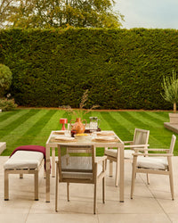 Minori natural wood dining set with table, chairs, and bench on patio, styled with place settings and centerpiece against manicured garden.