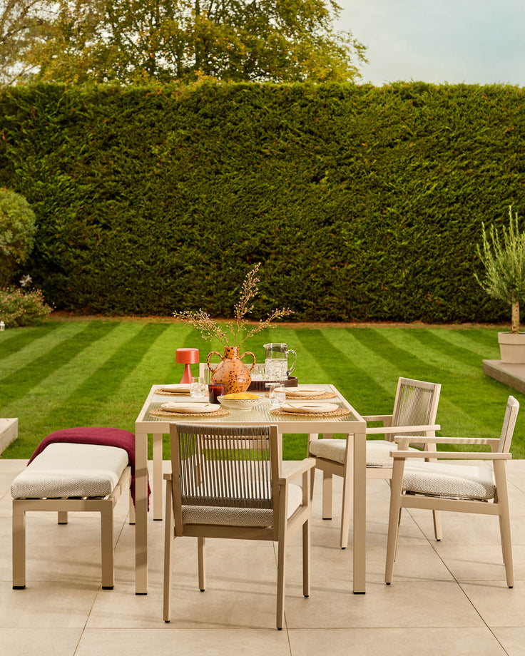 Minori natural wood 6-seater dining table with glass top, set on patio with chairs and benches in garden setting.