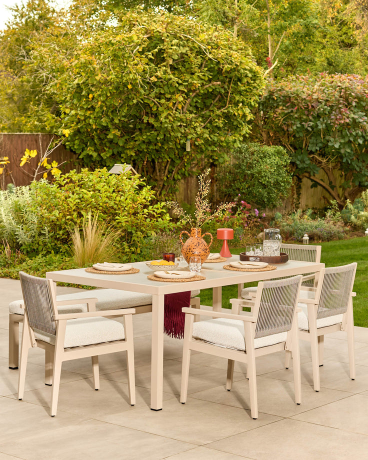 Minori natural wood 6-seater dining table with glass top, set with place settings and decorative items in a garden patio setting.