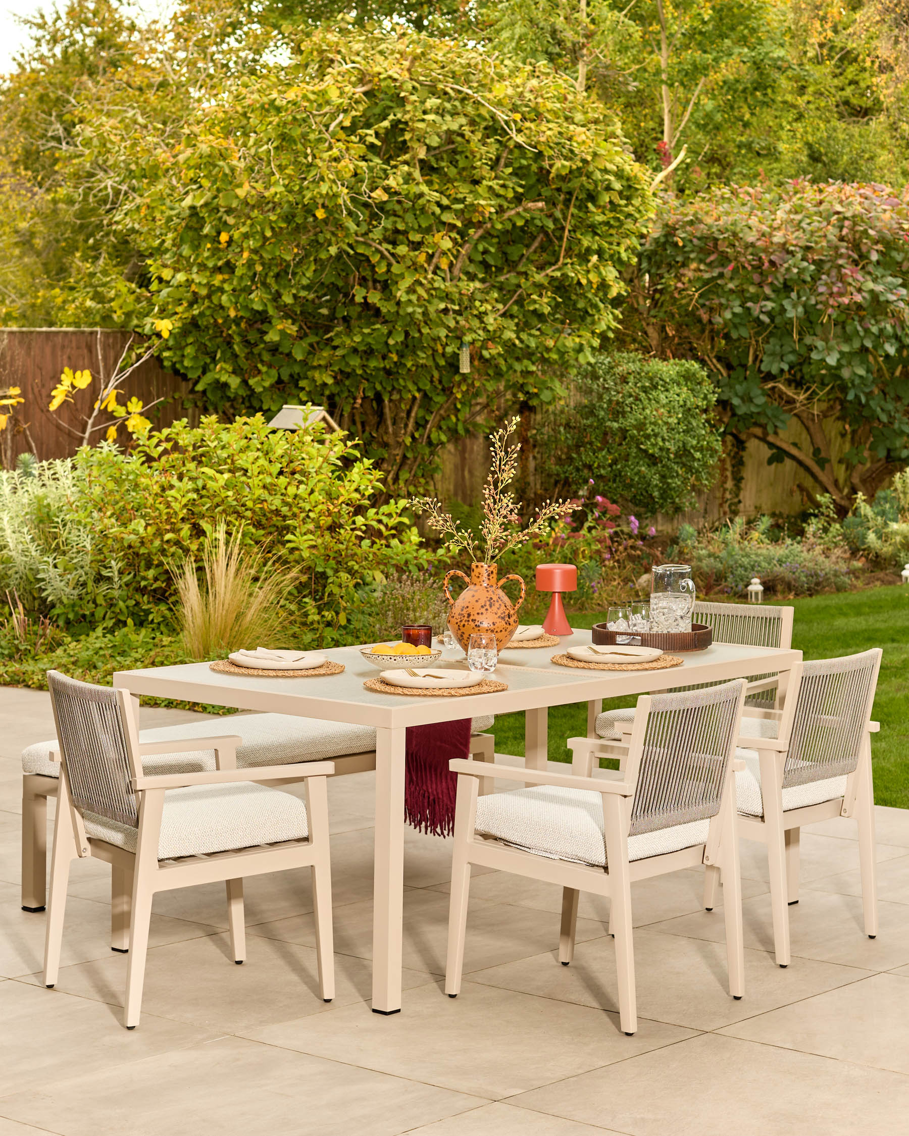 Minori natural wood garden dining bench with cream fabric cushion, shown in outdoor patio setting with matching dining chairs and table.