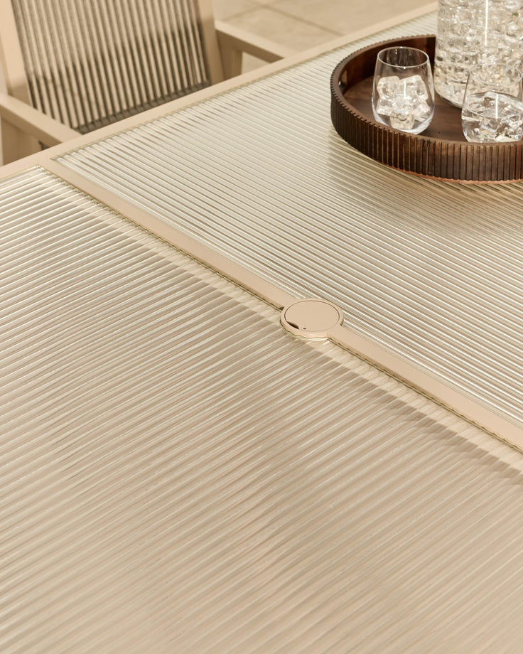 Cream ribbed dining table with integrated circular handle detail, glass top visible, modern minimalist design.