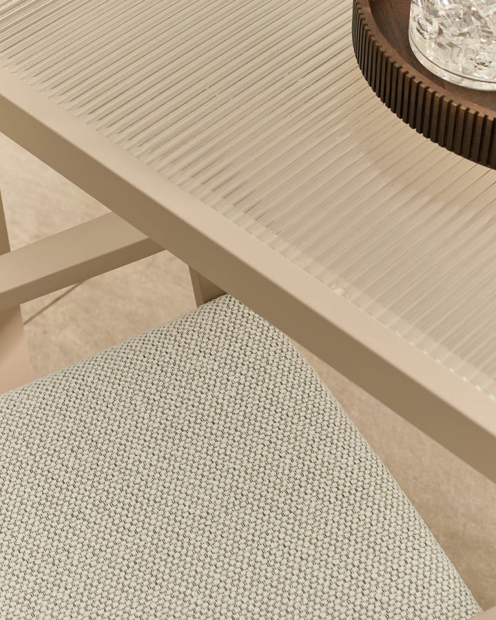 Cream-colored dining table with ribbed surface texture and glass top detail, angled view showing natural finish.