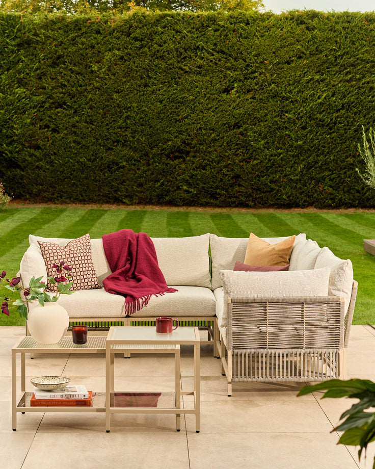 Minori large corner garden bench in natural finish with cream cushions, styled in a patio setting with accessories.