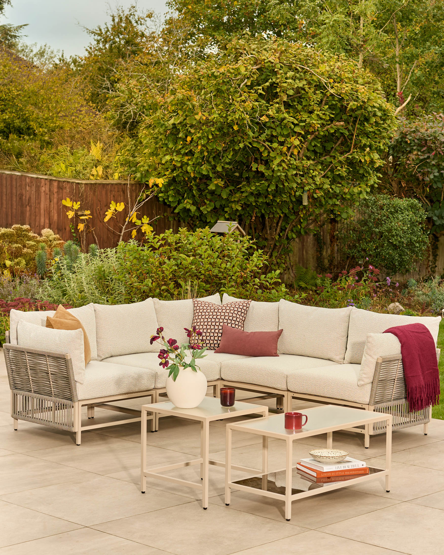 Minori natural garden corner bench and coffee table set with cream cushions on outdoor patio, styled with accessories.