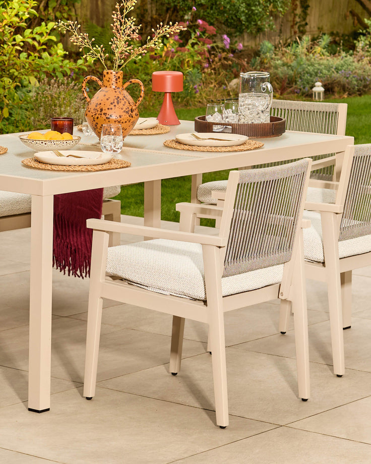 Minori cream garden dining table set for six with woven chairs, styled with tableware and decorative accessories on a patio.