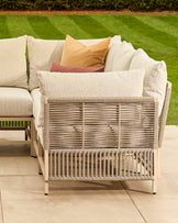 Minori garden large corner bench in natural finish with woven rope detailing, cream cushions, and decorative pillows on patio.