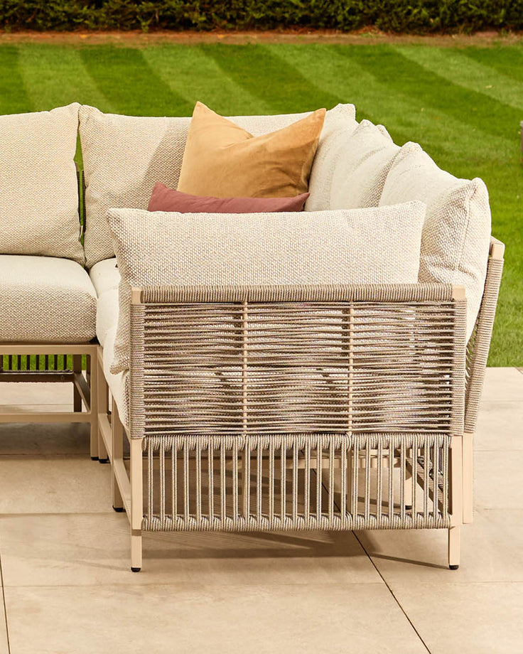 Minori garden large corner bench in natural finish with woven rope detailing, cream cushions, and decorative pillows on patio.