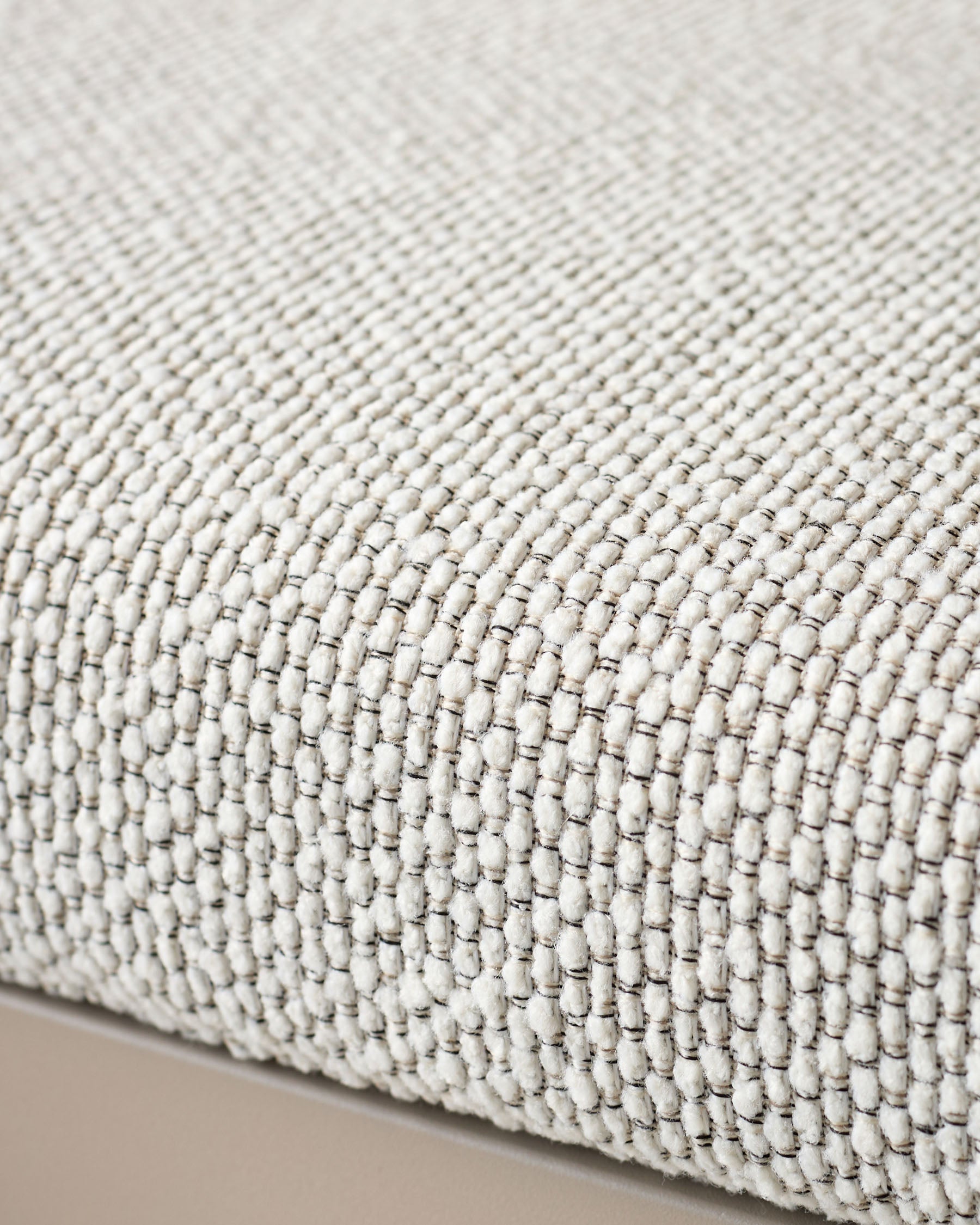 Close-up of natural cream woven fabric texture on dining bench seat with subtle gray stitching detail.
