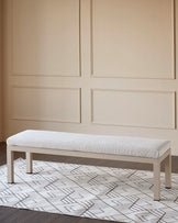 Minori Garden natural wood dining bench with light gray upholstered seat, displayed in a styled room with patterned area rug.