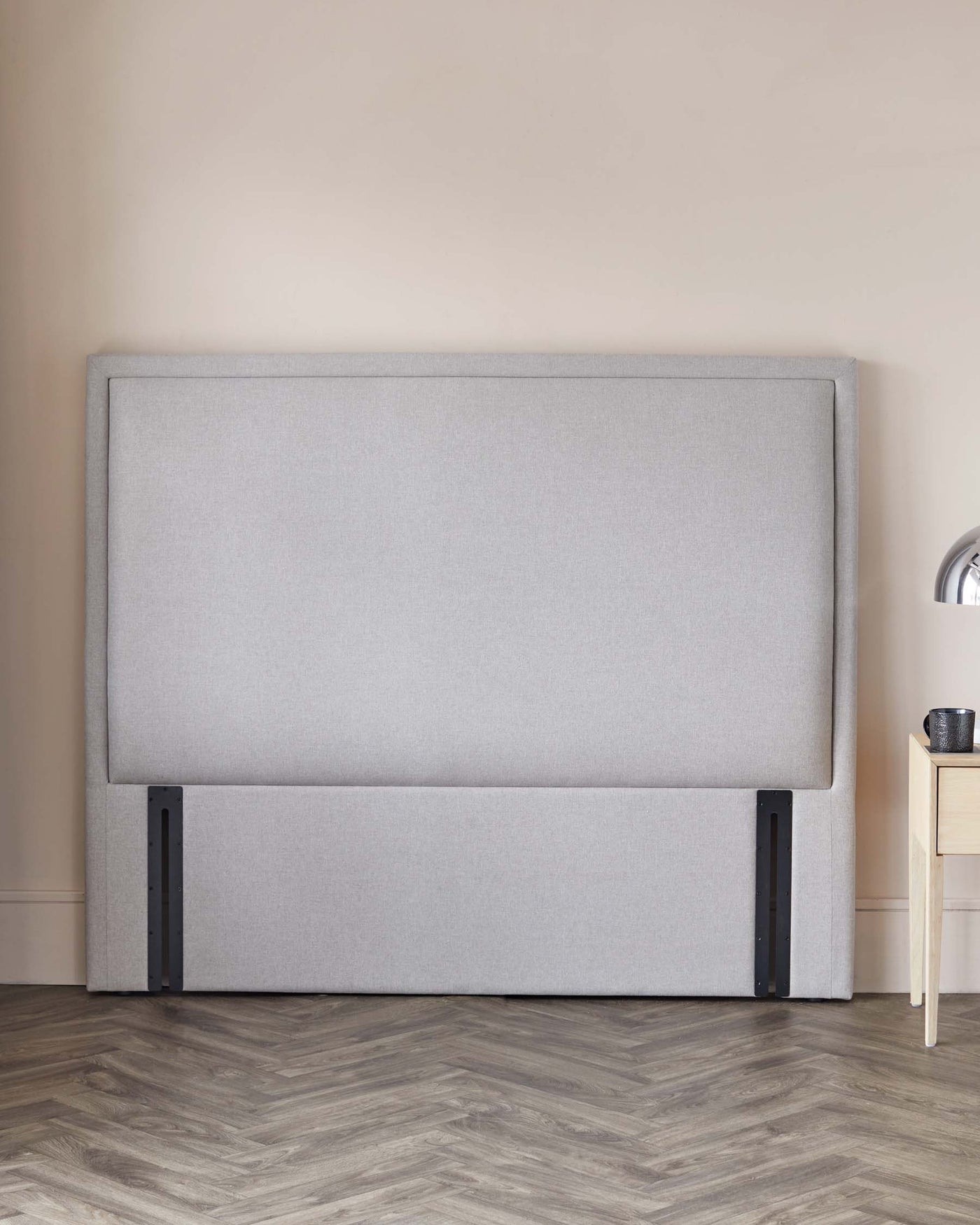 Contemporary grey upholstered headboard with a minimalist design and black metal legs, accompanied by a light wooden bedside table with a black vase.