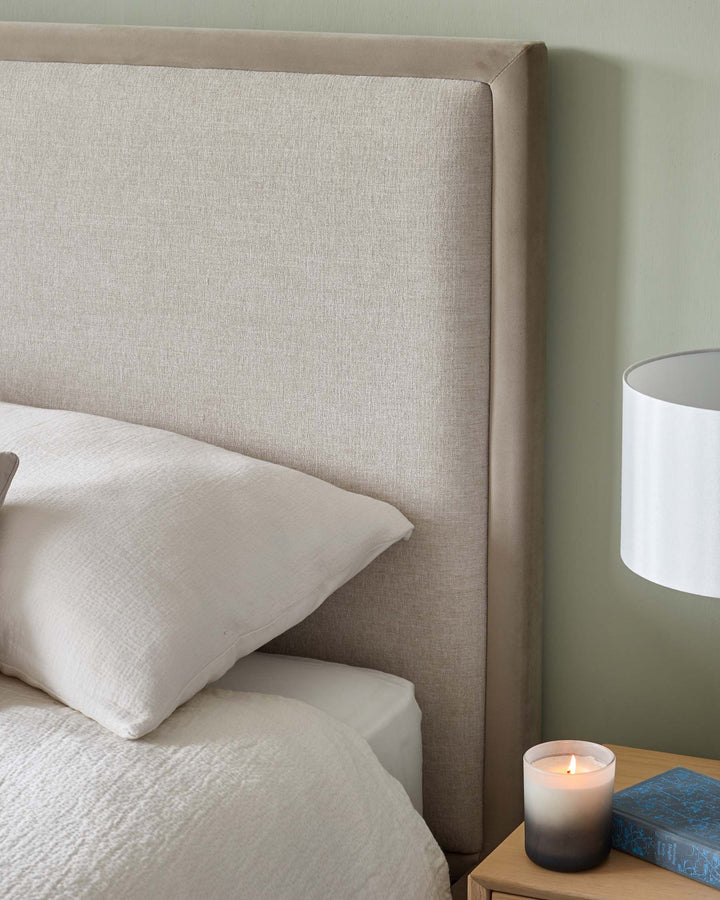 Upholstered headboard and bedside table with lamp, candle, and book. Cosy bedroom interior.