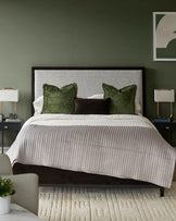 Bedroom with a bed with olive green and brown pillows, with bedside tables and a patterned rug.
