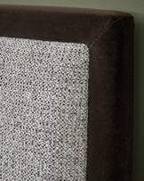 Close-up of a bed headboard with a dark brown velvet frame and a textured fabric panel.