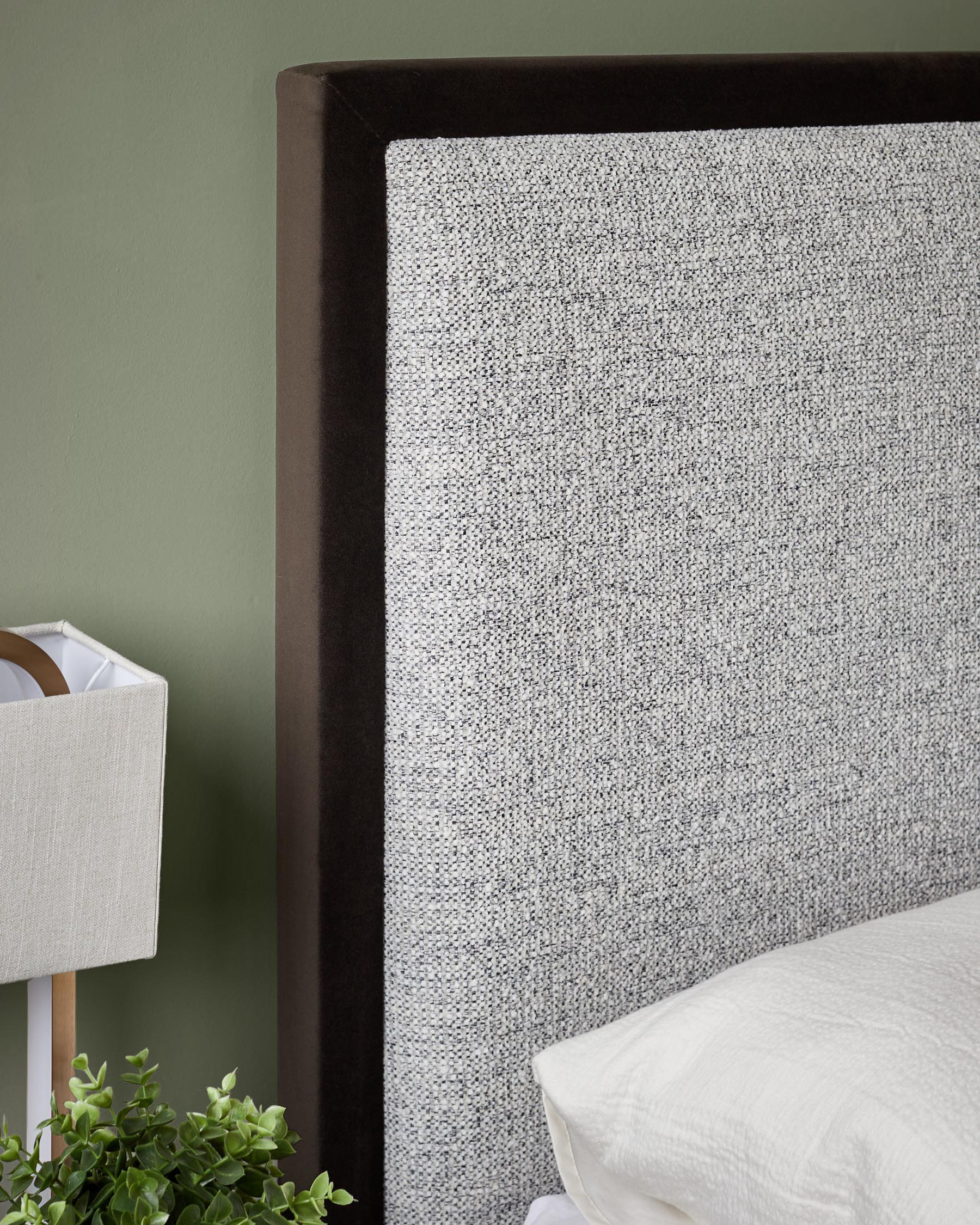 Upholstered headboard in grey fabric with a dark brown trim, on a bed with white bedding, with a lamp on the side table.