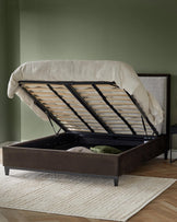 An open, brown upholstered storage bed is the focus, featuring a beige throw and neutral rug.