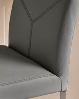 Close-up of a grey, leather dining chair with stitched detailing and a metallic frame, showcasing its modern design.