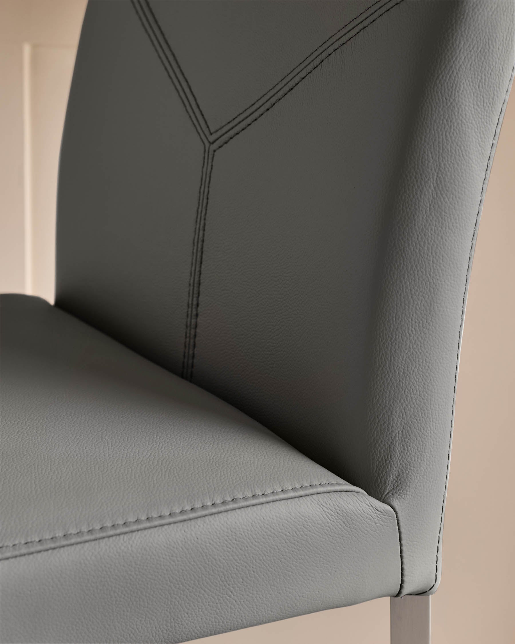 Close-up of a grey, leather dining chair with stitched detailing and a metallic frame, showcasing its modern design.