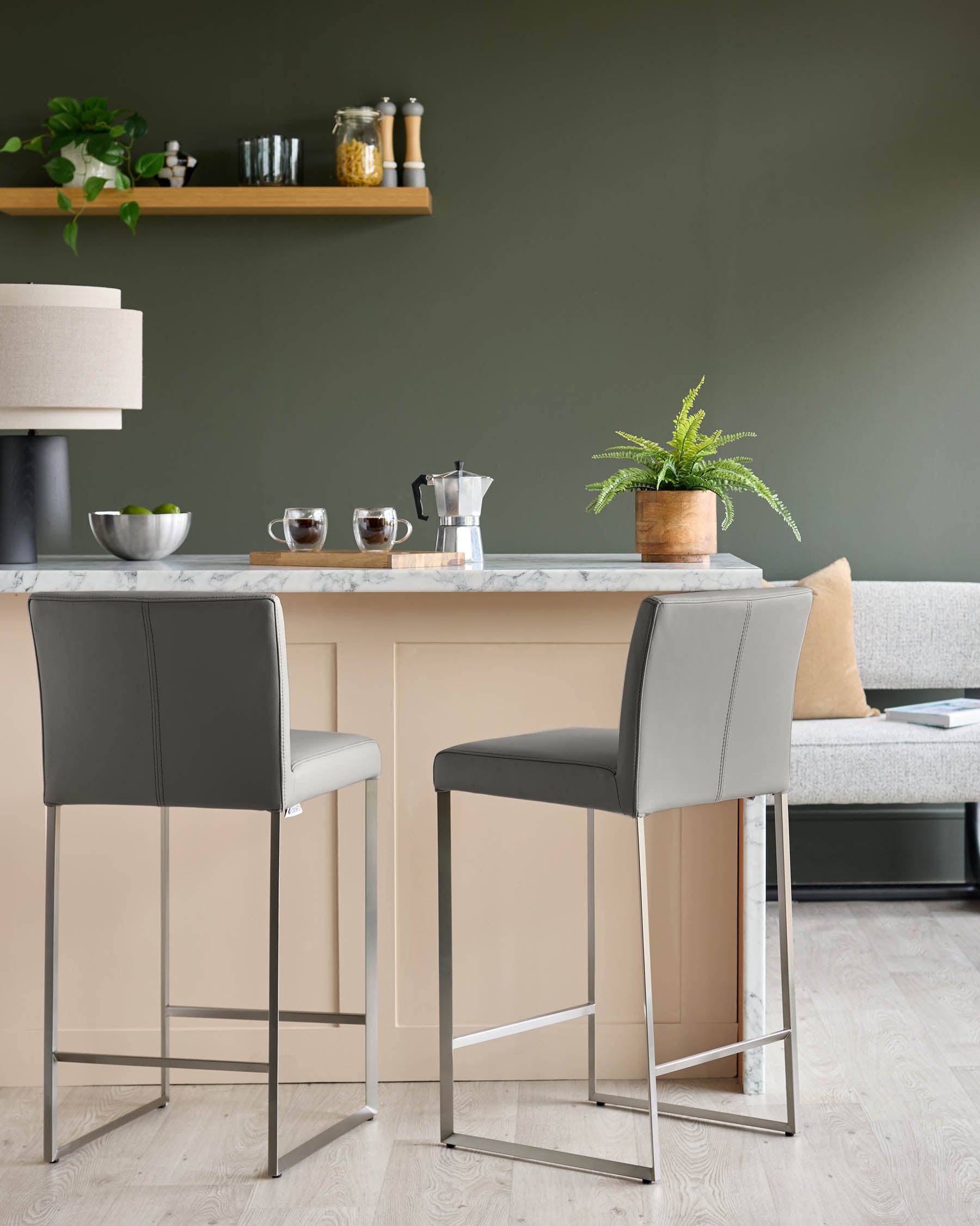 Two grey bar stools with metal legs at a kitchen island with a marble countertop and green walls.