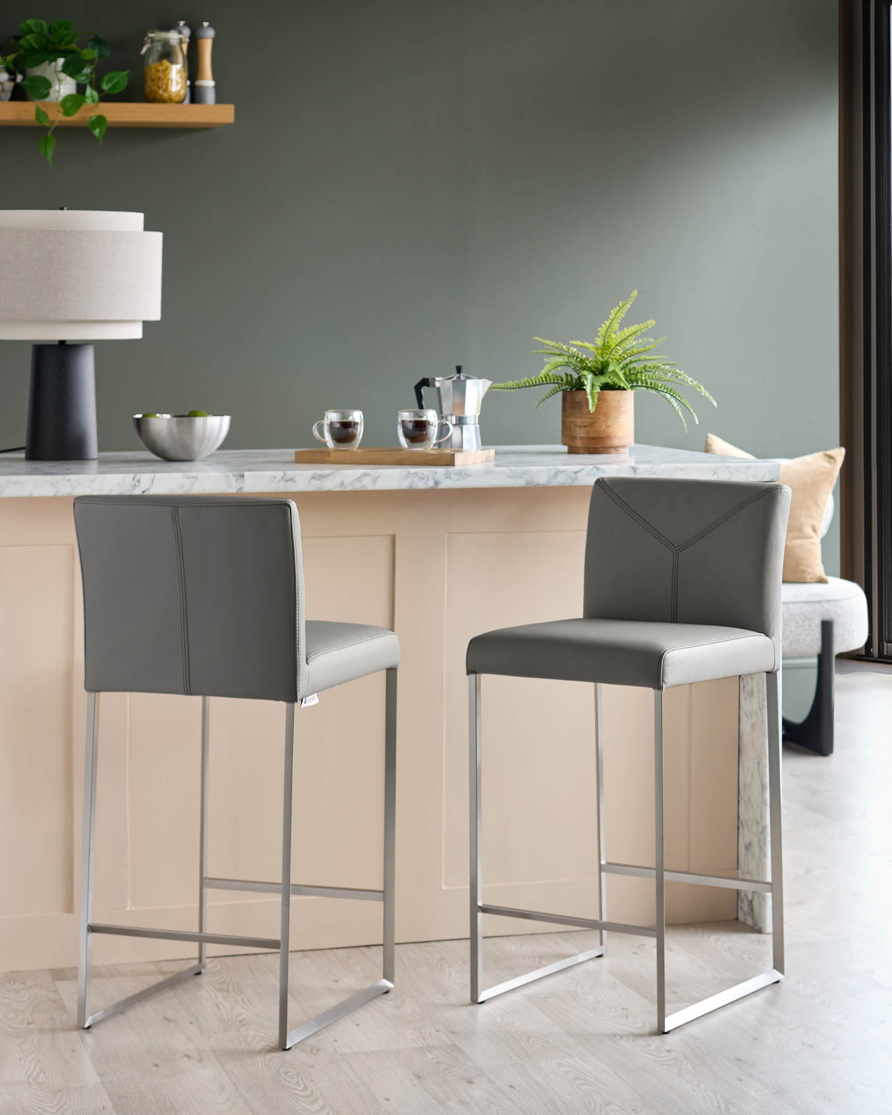 Two grey bar stools with a metal frame stand at a kitchen counter.