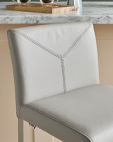 A contemporary grey leather bar stool with stitching detail, set against a kitchen countertop.