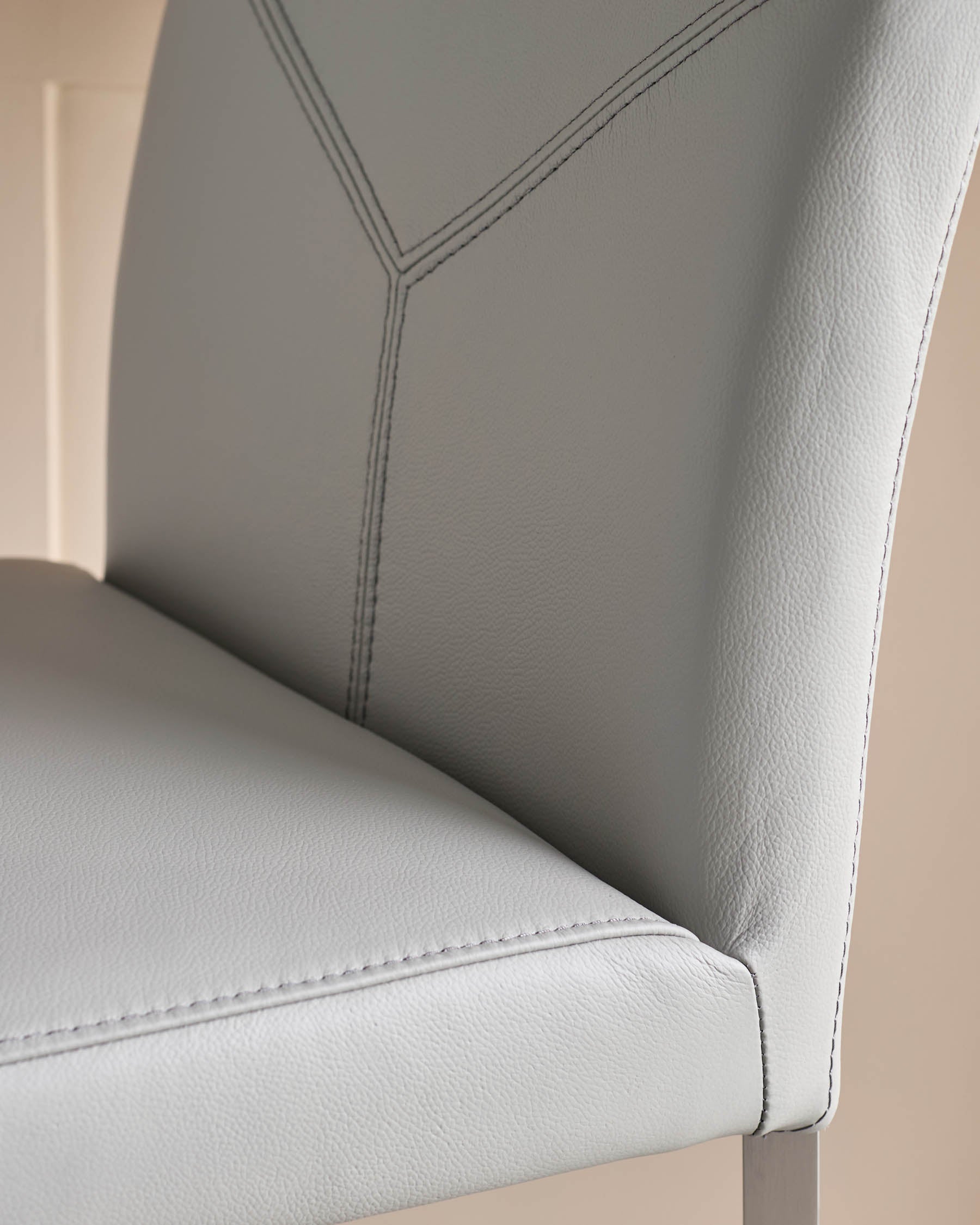 Close-up of a stylish, grey leather chair with intricate stitch detailing. Perfect for modern dining or kitchen spaces.