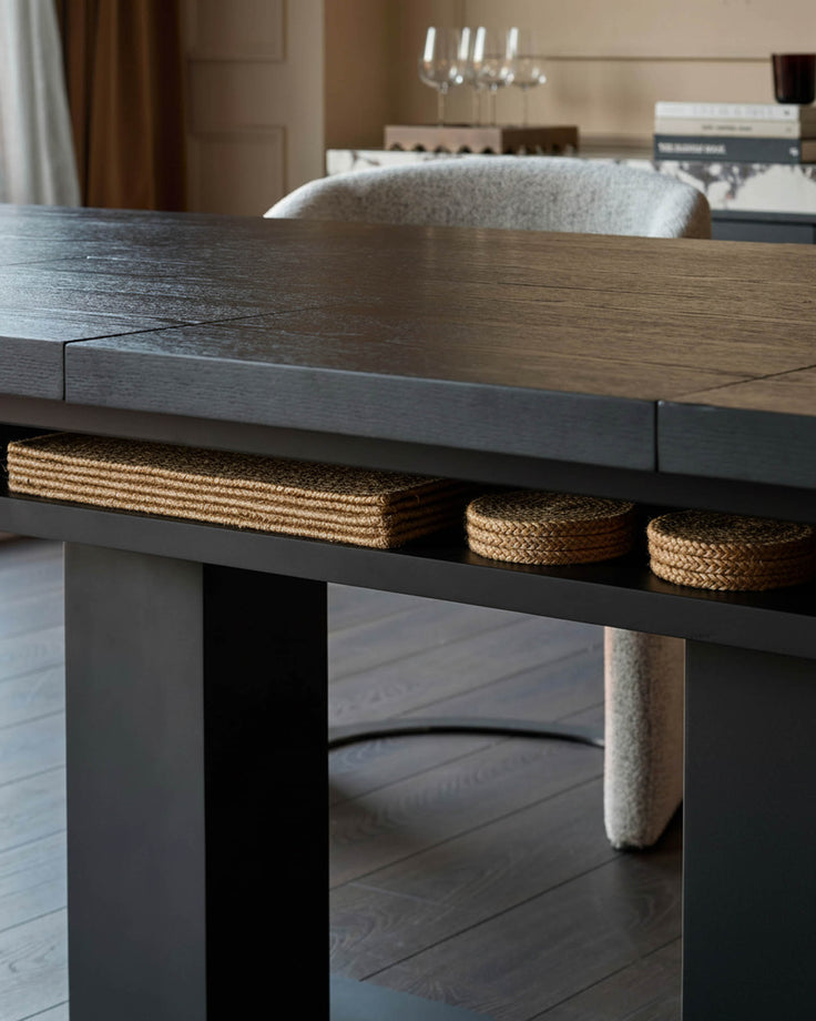 Dark wood dining table with woven storage baskets on lower shelf and upholstered seating visible in background.
