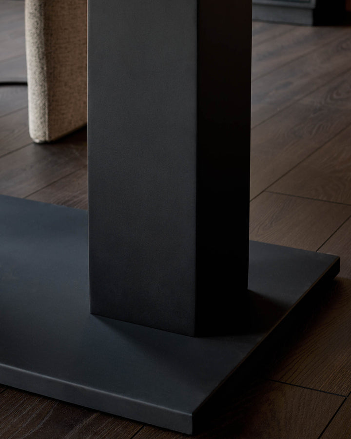 Dark wood dining table base detail showing black metal support column and foot on wood flooring.