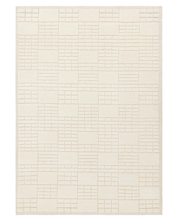Ivory-coloured area rug with a geometric block pattern and textured details, finished with a fringe edge.