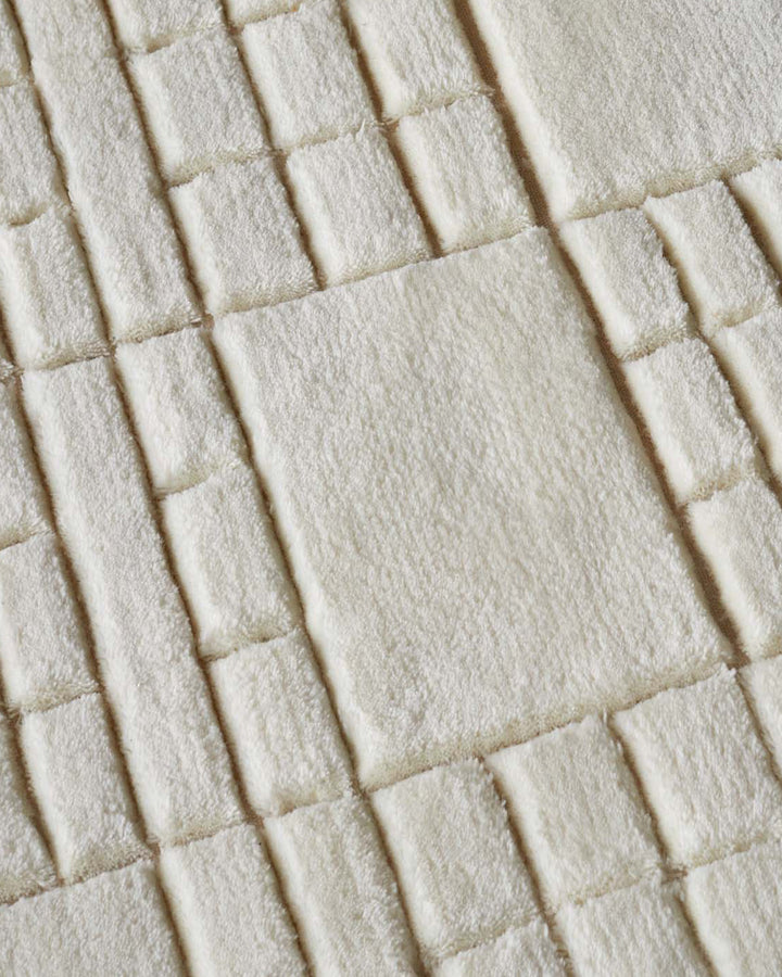 Close-up of cream wool rug with sculpted mosaic tile pattern and dimensional texture.