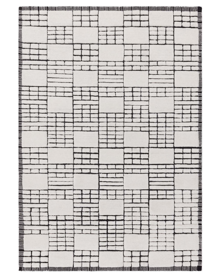 Modern area rug with geometric block pattern in black and white, featuring a fringe detail at the edges.