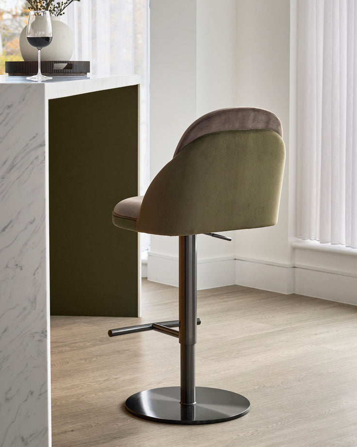 Myra gas lift bar stool in mocha and olive green velvet, shown from side angle with black metal base in modern room setting.