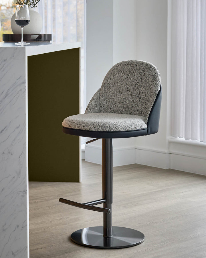Myra gas lift bar stool in grey fabric and black faux leather, featuring a rounded backrest and black metal base with footrest.
