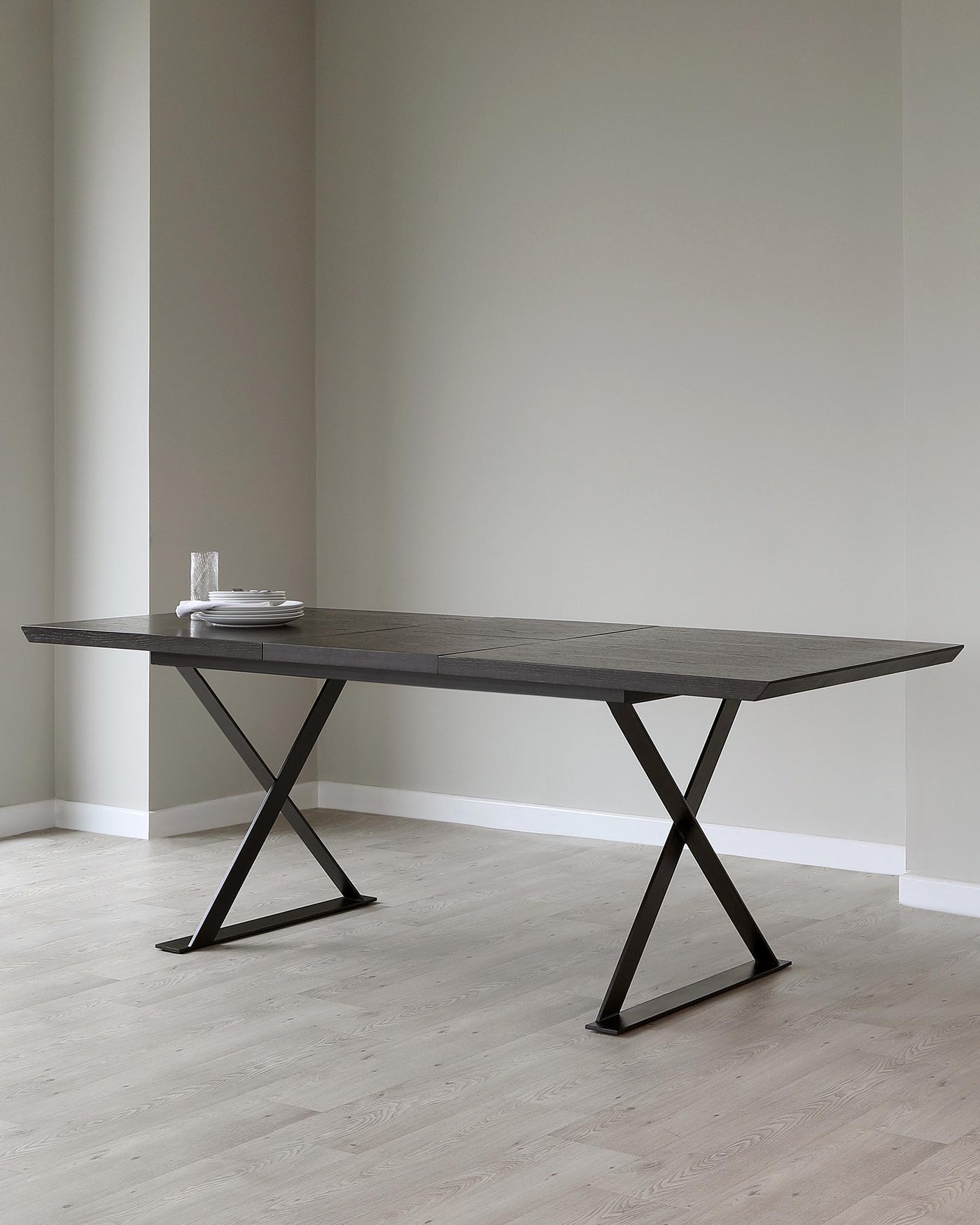 Modern minimalist dining table with a dark wood finish and distinctive X-shaped metal legs in a minimalist interior.