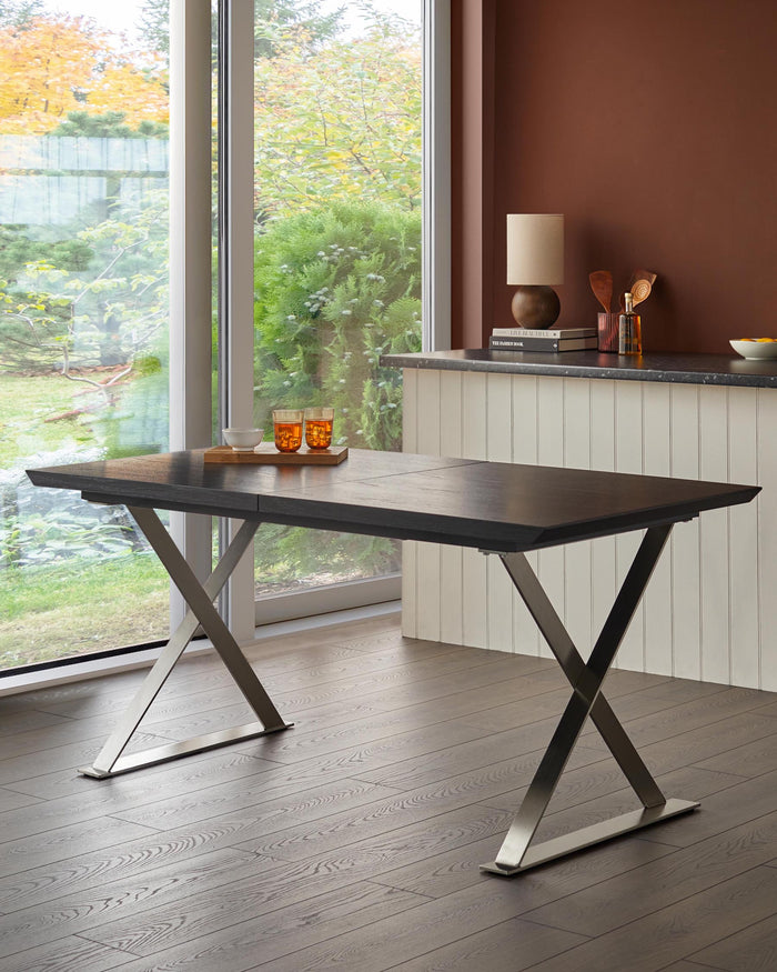 A dark wood dining table with a chrome 'X' shaped base, styled with glasses and a bowl.
