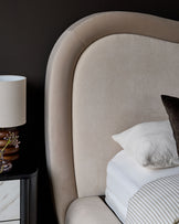 Naomi king-size ottoman bed in champagne velvet with curved headboard and white bedding, styled with bedside lamp.