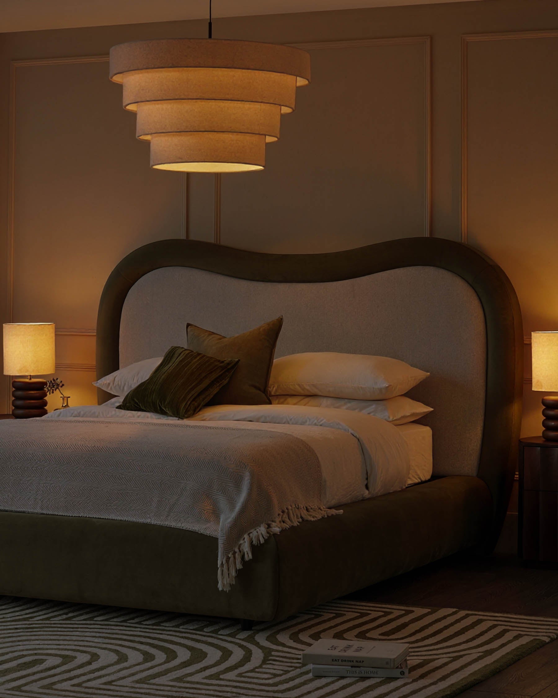 Naomi king-size ottoman bed in olive-green velvet with curved headboard, styled in warm bedroom setting with pendant light and bedside lamps.