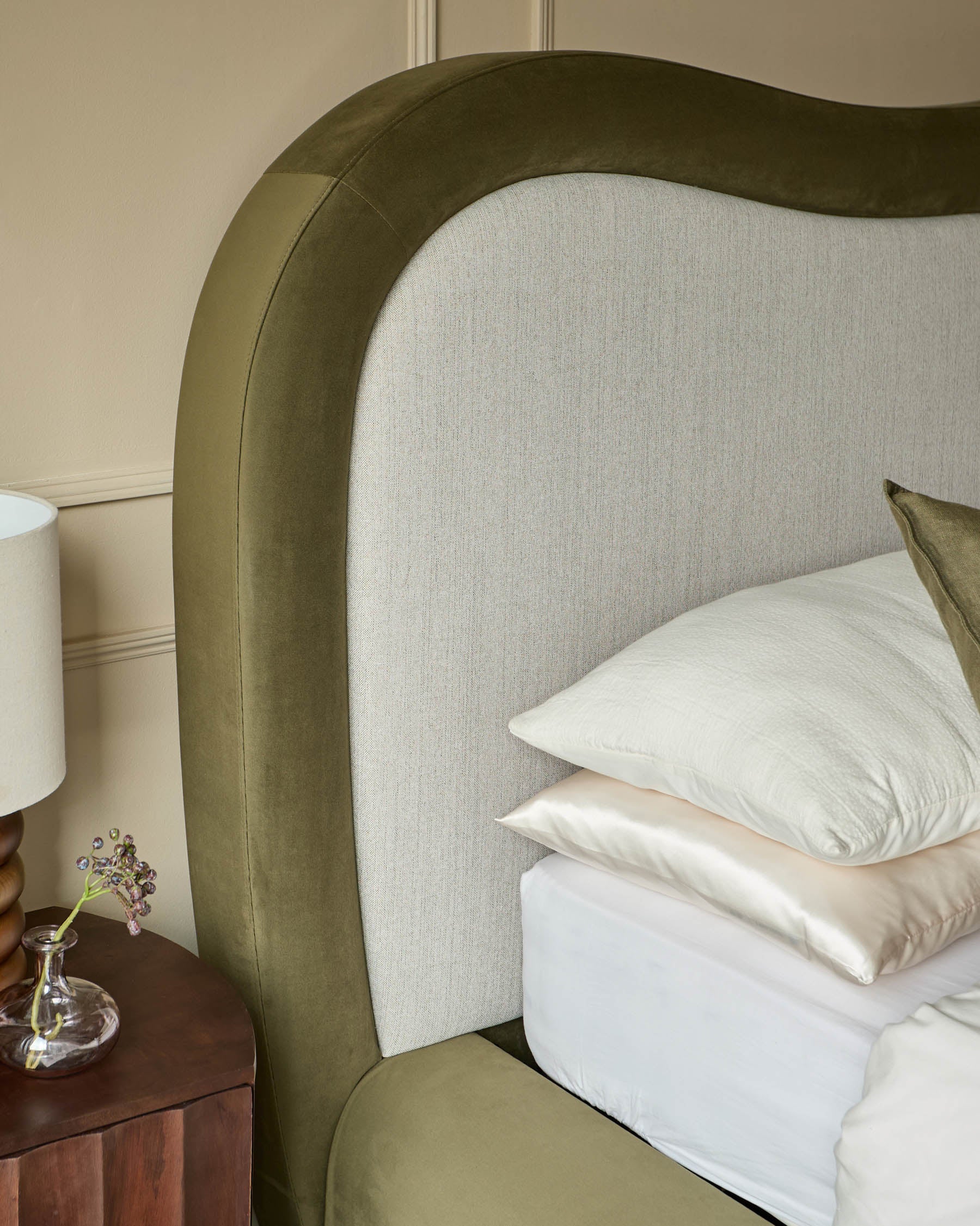 Naomi king-size ottoman bed in olive green velvet with natural linen headboard, styled with white bedding and nightstand.