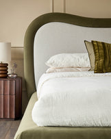 Naomi king-size ottoman bed in olive-green velvet with curved headboard and cream bedding in bedroom setting.