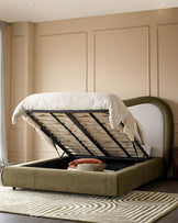 Naomi King-Size Ottoman Bed in olive-green velvet with storage compartment open, showing wooden slat base and white bedding.
