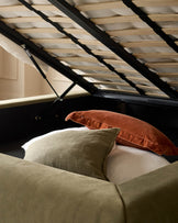 Naomi king-size ottoman bed in olive-green velvet with natural wood slatted headboard, open storage base visible.
