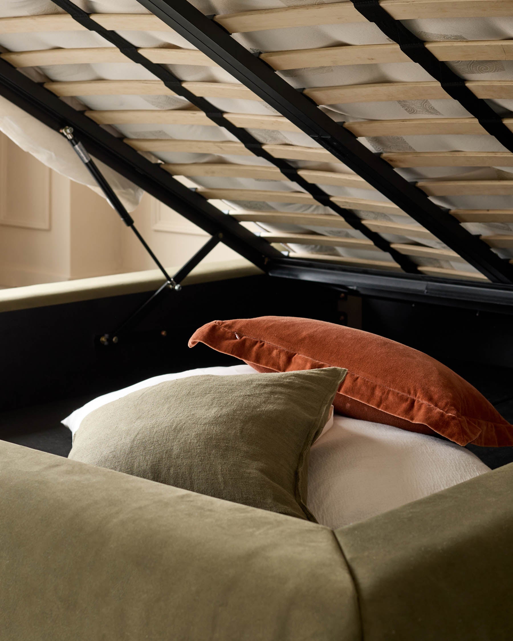 Naomi king-size ottoman bed in olive-green velvet with natural wood slatted headboard, open storage base visible.
